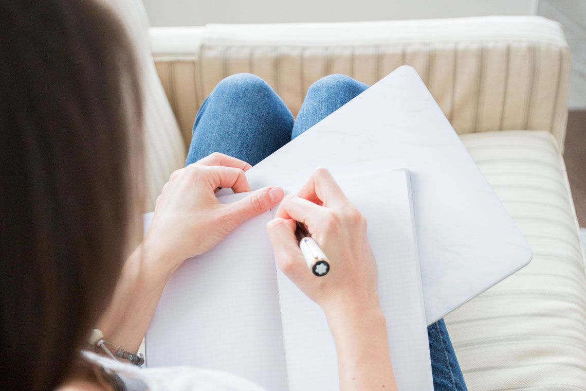 Frau sitzt auf der Couch und macht Notizen